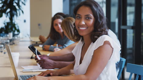 Portrait-Of-Businesswoman-Working-At-Desk-On-Laptop-In-Shared-Open-Plan-Office-Workspace