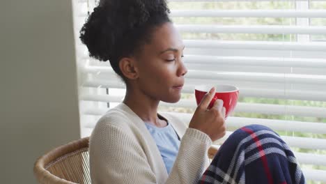 Video-of-thoughtful-african-american-woman-drinking-coffee-and-looking-outside-window