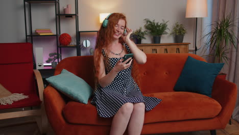 chica feliz y relajada con auriculares inalámbricos bailando escuchando su música rock n roll favorita en el sofá de casa