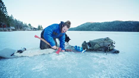 un tipo pescando en invierno rompiendo el hielo del agujero de un río congelado usando un hacha en noruega
