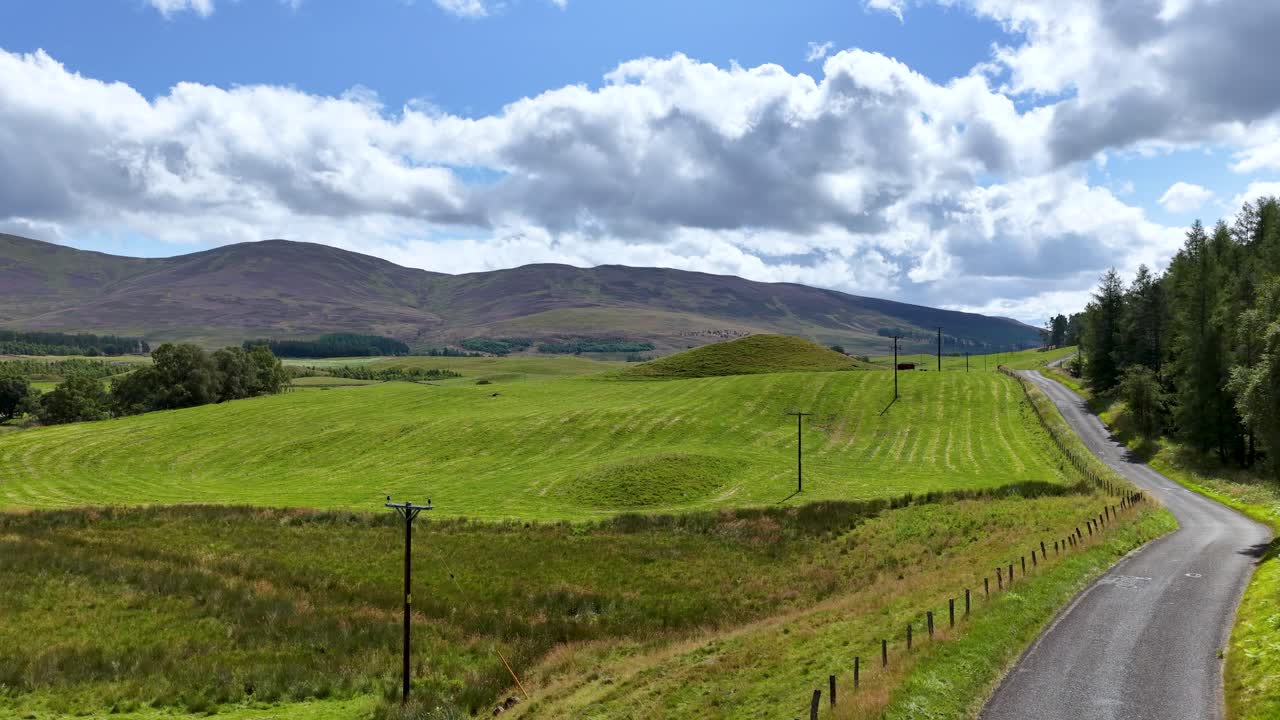 Sunny daytime drive through lush green meadows, rolling hills, and winding rural road, steady camera