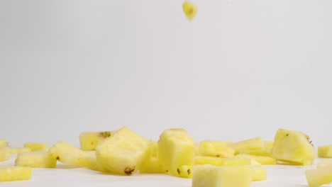 fresh yellow chopped pineapple chunks falling and bouncing into a pile on white table top in slow motion