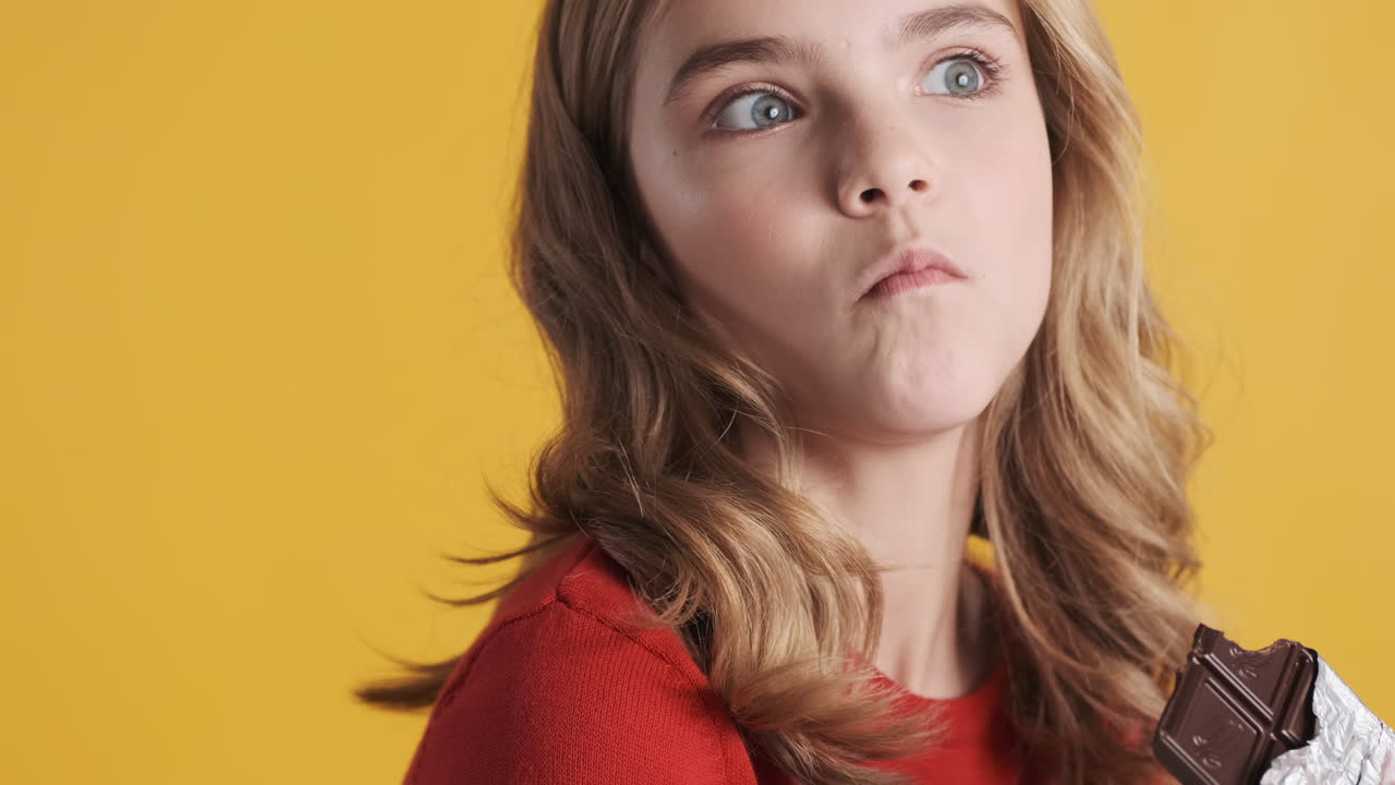 십대 백인 소녀가 초콜릿 바를 먹고 고개를 끄덕인다.