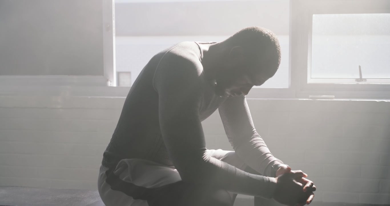 Checking watch, African American man sitting on bench by window adjusting wraps, preparing to train