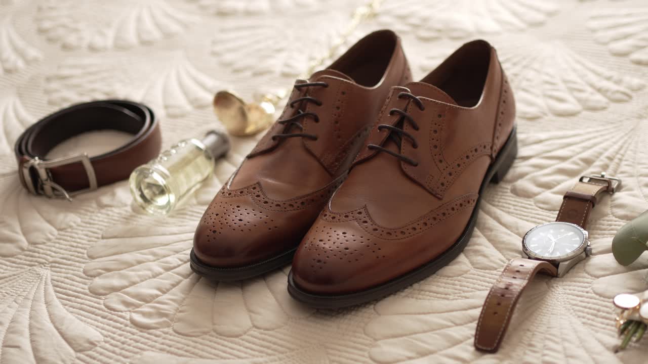 Close up of groom's wedding accessories featuring leather shoes, belt, watch, and perfume