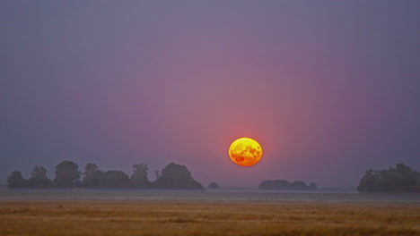 Supermond-Steigt-über-Einem-Bauernhoffeld-Mit-Einer-Niedrigen-Nebel--Oder-Nebelschicht-Auf,-Um-über-Die-Landschaft-Zu-Glühen---Zeitraffer