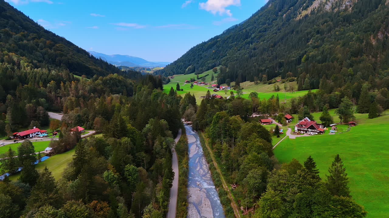 Narrow river crossing the stunning valley with some cottages in the Bavarian Alps. Breath-taking view of Oberstdorf, Europe from drone.