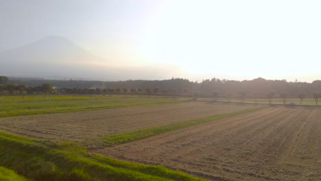 Toma-Aérea-Giratoria-Izquierda-Sobre-Campos-Agrícolas-Con-Silueta-Alta-Del-Monte-Fuji-En-La-Distancia