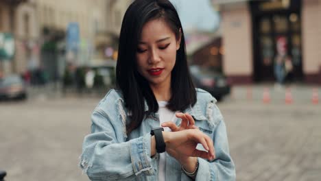 pretty young woman standing at the city center and tapping on the smartwatch on her hand on a summer day