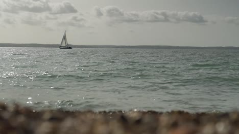 boat floats on the sea, with waves crashing into pebbles in the foreground