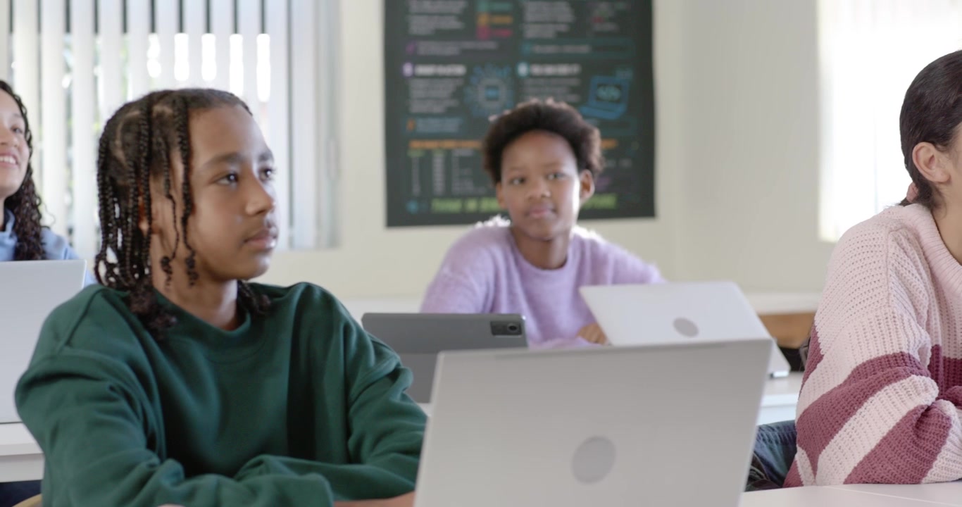 Class watching teacher talking, African American teen typing on laptop headset in class, copy space