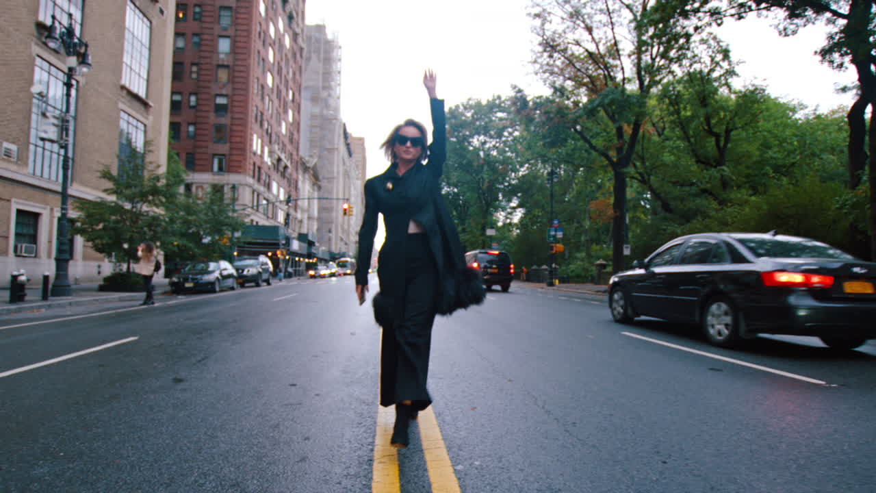 New York, USA, 25 maggio 2025: Donna in cappotto nero che cammina su una strada vuota di New York. Cappotto nero bordato di pelliccia che cammina lungo la linea gialla di una strada di Manhattan