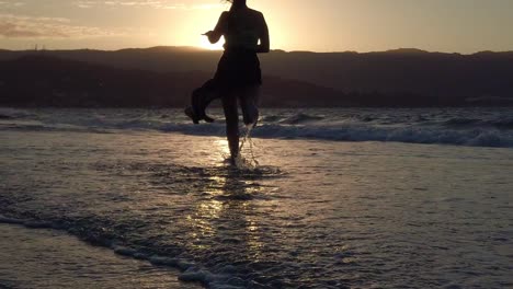 woman running in the sea shore towards the sunset in slow motion.