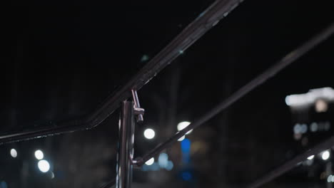 close downward view of a moist metal handrail at night, with water droplets glistening under soft lighting