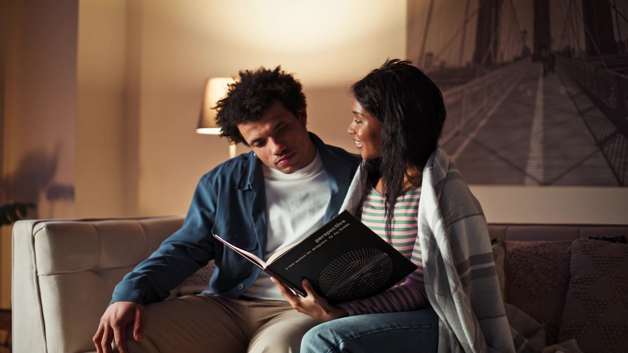 Cónyuges relajados leyendo un libro, acurrucados juntos en el sofá del apartamento, primer plano