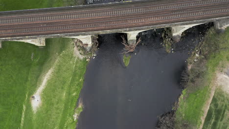Aerial-Birds-Eye-View-of-Train-Tracks-Crossing-River-in-Yorkshire,-England-in-direction-of-Water-Flow