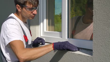 Man worker in safety glasses cleaning surface for PVC window metal sill installation