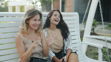 two women friends having a conversation on a park swing