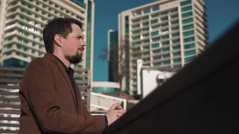 thoughtful man is leaning on stone fence in city in sunny day, breathing air