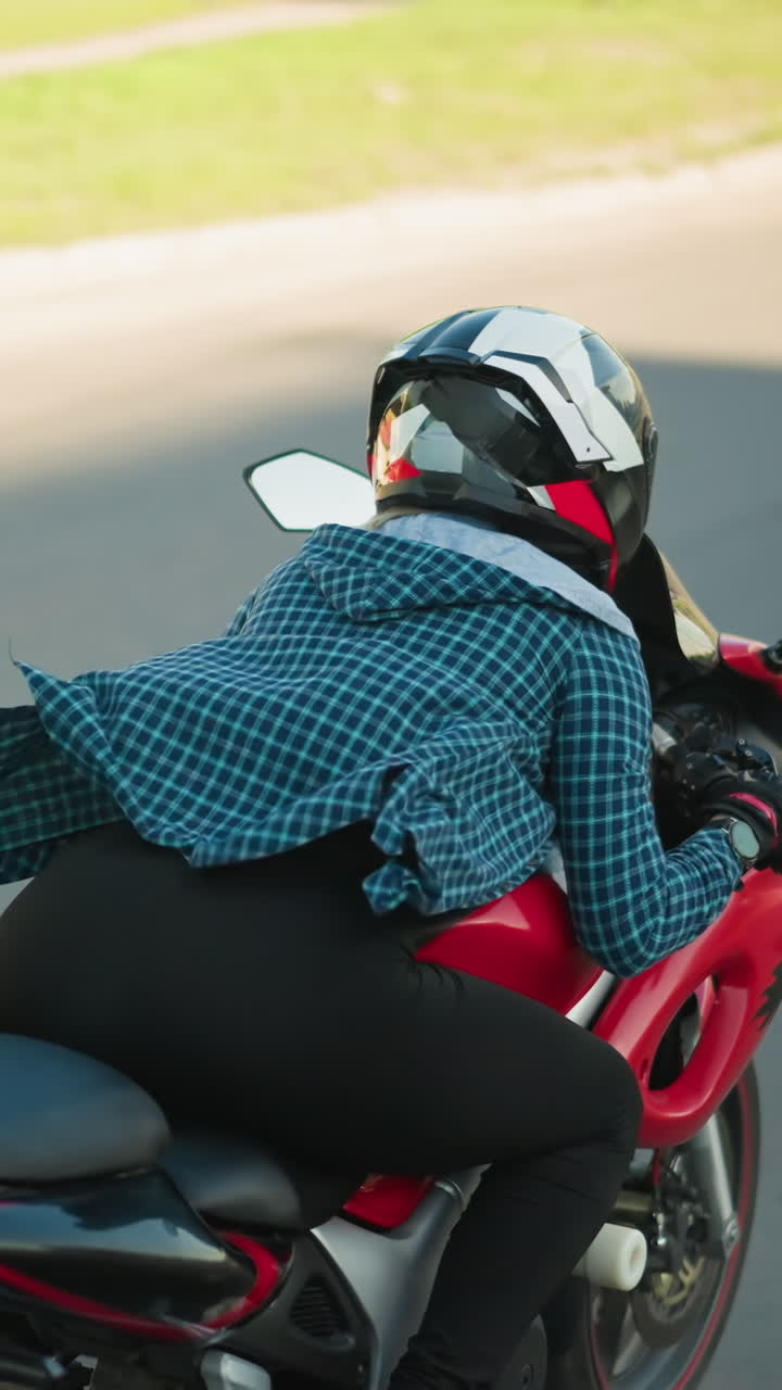 한 여성 오토바이 운전자가 빨간색 파워바이크를 타고 앞으로 기울어서 도시 도로에서 파란색 버스와 색 차를 뛰어넘으며, 그녀의 체크 된 셔츠가 바람에 날아갑니다.