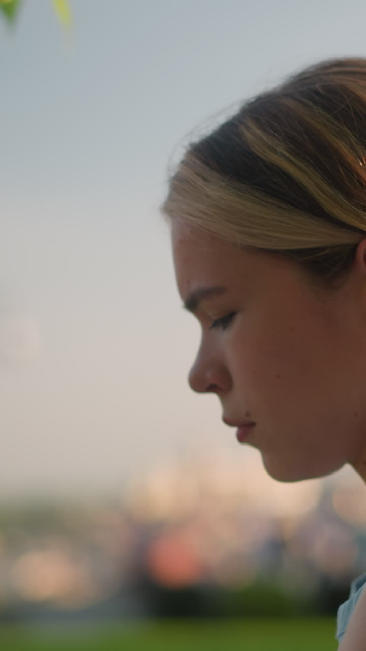 vista lateral de una joven que se ve pensativa mientras la luz del sol se refleja en su cara, con un movimiento gracioso como patinaje, el fondo natural borroso incluye vegetación, árboles y un paisaje urbano sutil en la distancia
