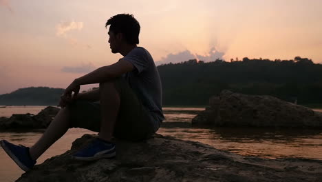 Man Sitting by River at Sunset