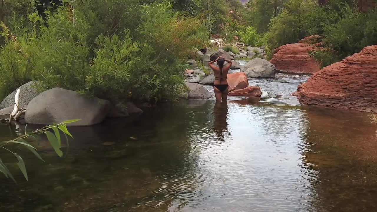 Mujer de pie en el agua del río, toma de naturaleza en cámara lenta posando con las manos sobre la cabeza