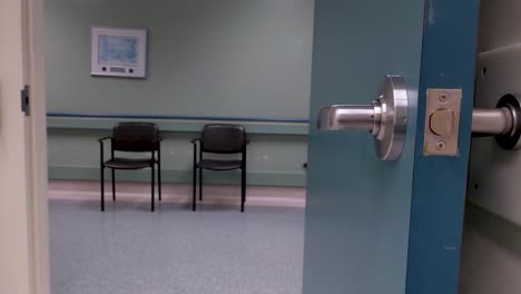 two chairs seen through an open doorway in an empty hospital corridor as camera pans left.