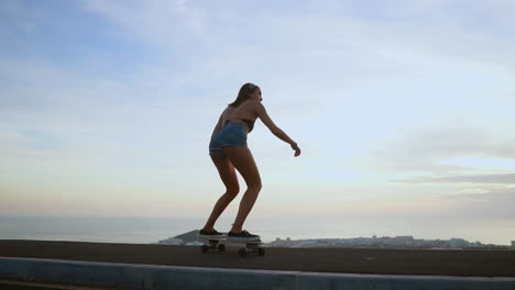 With-the-mountains-in-the-background,-a-stylish-young-skateboarder-rides-her-board-in-shorts-on-a-mountain-road-at-sunset,-all-captured-in-slow-motion