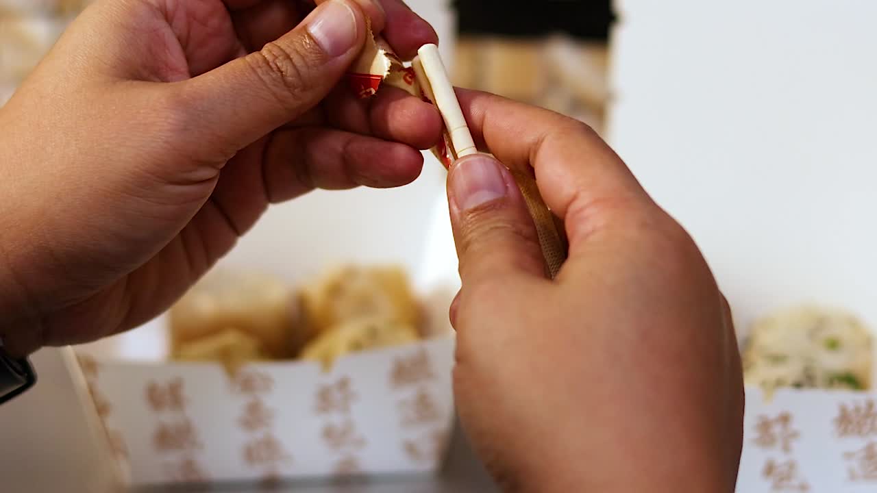 Un primo piano di mani che aprono con cura una confezione di carta per rivelare delle bacchette di legno