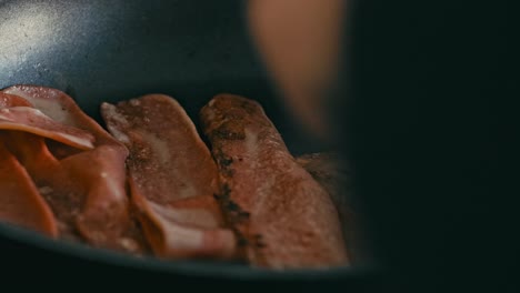 el primer plano captura a una persona usando un tenedor para voltear el tocino chisporroteante en la sartén