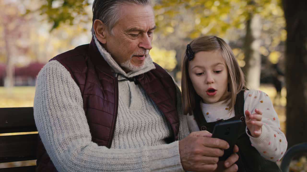 Caucasian grandfather with girl using mobile phone at the park