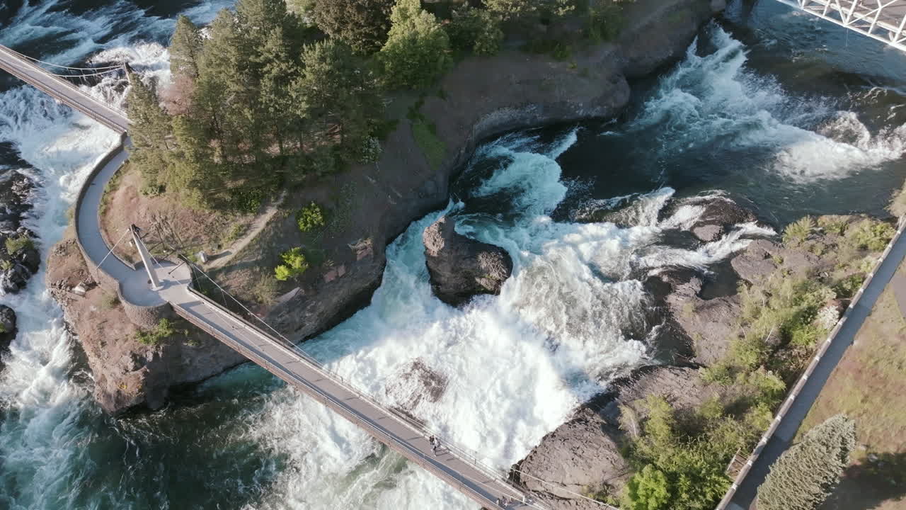 Bridges and walkways cross over Spokane Falls in the heart of the city. Water rushes around a tree-covered island