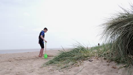 Young-boy-in-a-wetsuit-on-a-beach-digging-in-the-sand