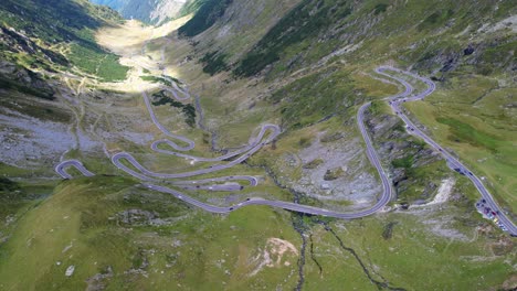 cars quickly drive switchback winding busy road of transfagarasan serpentine highway in romania, under shadow of mountain peaks