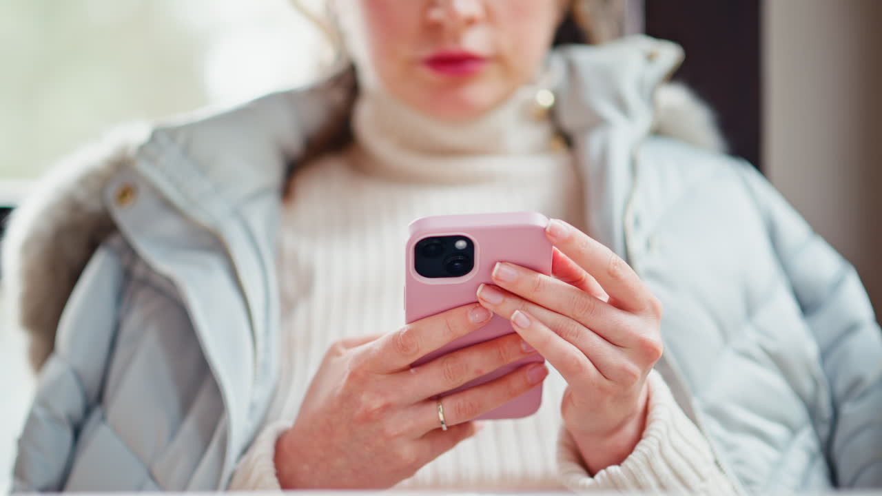 Woman in jacket scrolling through her phone at a cafe