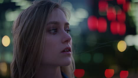 retrato de cerca mujer joven rubia atractiva que parece pensativa disfrutando de la tranquila vida nocturna urbana en la ciudad por la noche el viento soplando el cabello cámara lenta serie de personas reales