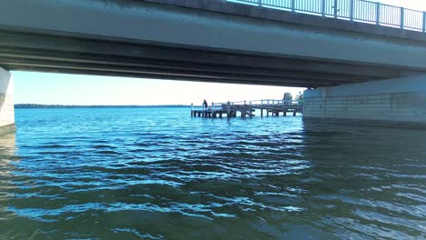 drone aerial shot of person fishing off dock wharf pier with cars driving on overpass bridge street toukley gorokan central coast australia