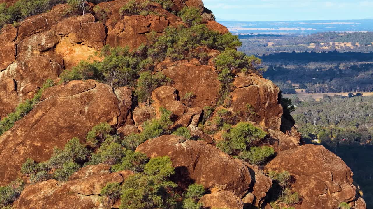Drone glides past rugged volcanic outcrop with sandstone boulders, warm sunset light, wide landscape