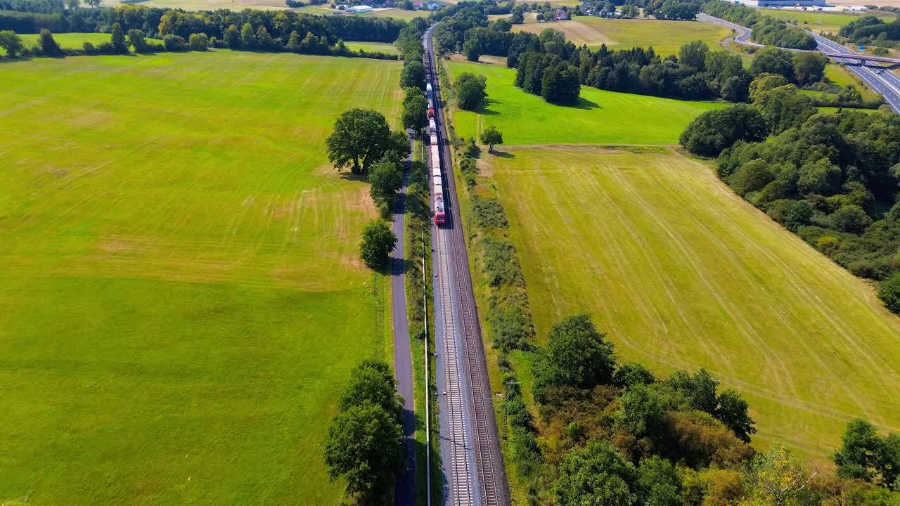Freight Train Moving Along Railway Tracks Through Green Countryside Fields Captured by Drone