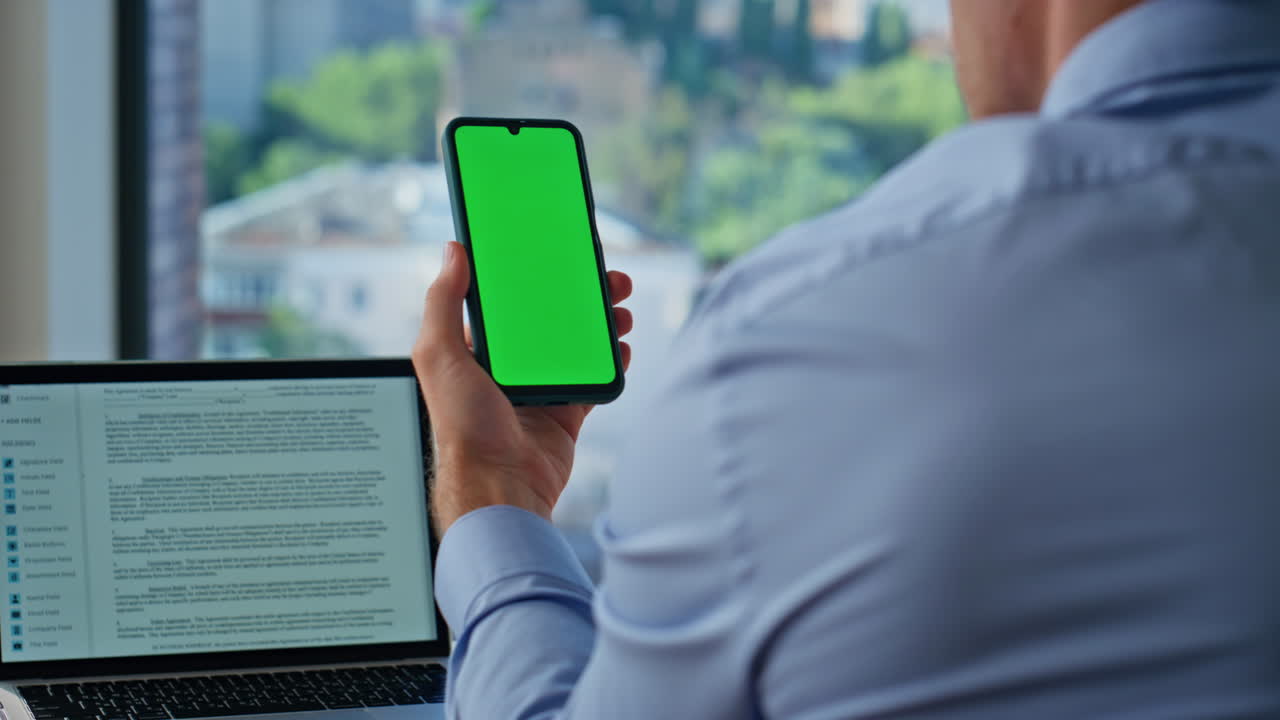 Businessman browsing greenscreen cellphone in corporate office closeup back view
