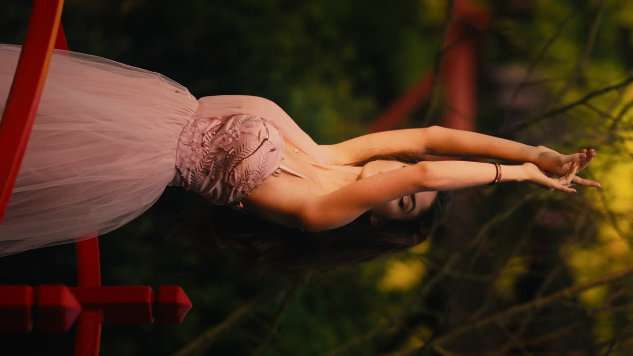 hermosa mujer joven en vestido rosa, brazos levantados al cielo, pose sensual, de pie en un puente de madera rojo, bosque, cámara lenta, vertical