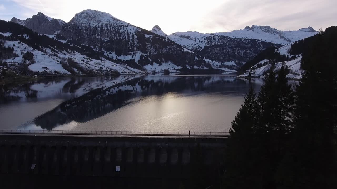 gran panorama de montaña de invierno en un lago artificial con un tipo en la presa en suiza