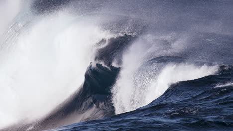 Eine-Glasige-Welle-Rauscht-In-Zeitlupe-An-Einem-Flachen-Felsvorsprung-Entlang,-Während-Der-Ablandige-Wind-Gischt-Zurück-An-Die-Wellenwand-Bläst