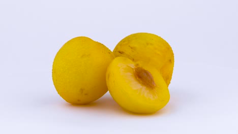 two whole and one half cut of a big yellow mirabelle plums with water drops. slowly rotating on the turntable isolated on the white background. close-up