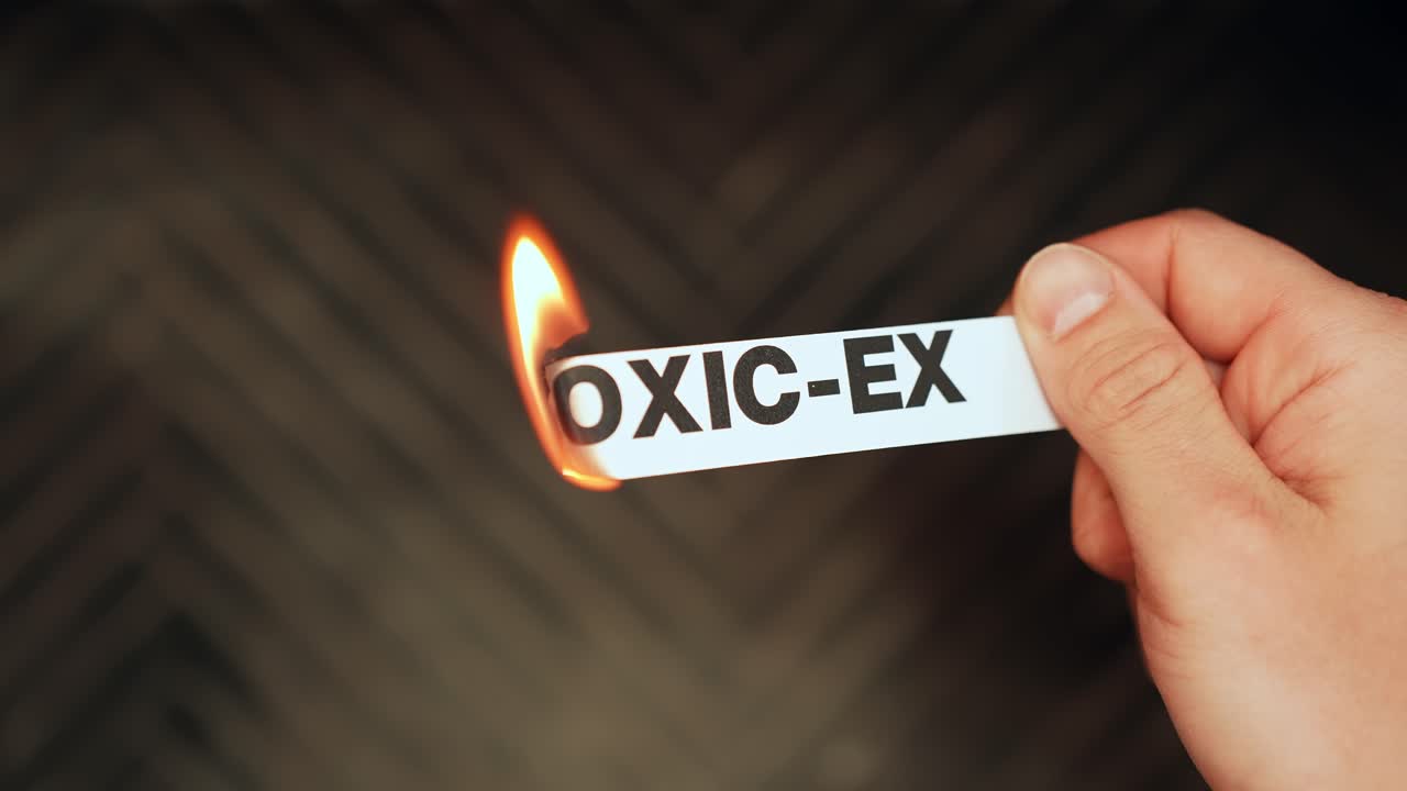 Hand holds a paper label reading TOXIC-EX while a flame burns the edge, symbolizing breakup, boundary setting, and leaving an unhealthy relationship