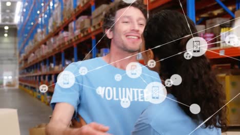 Animation-of-network-of-digital-icons-over-diverse-male-and-female-volunteers-hugging-at-warehouse