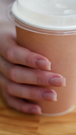 vista de cerca de la mano de la dama tocando la taza de café en la mesa de madera con el teléfono parcialmente visible y la caja de madera en el fondo, creando una atmósfera acogedora con un borrón suave
