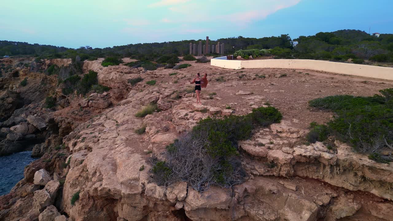 dancing Woman expressing freedom and movement by the sea at a beautiful travel destination Cala Llentia Ibiza. Fantastic aerial view flight overflight flyover drone