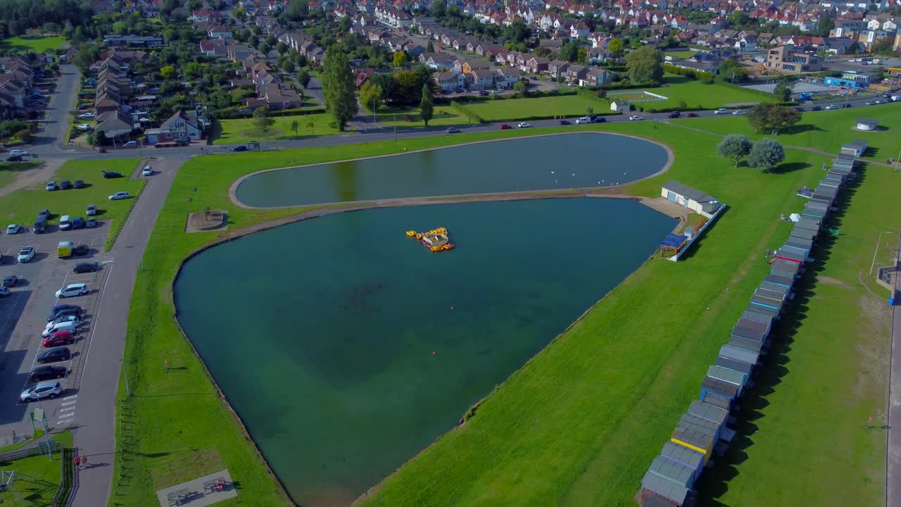 배경에는 다채로운 해변 오두막이 있는 도버코트 보트 호수의 드론 전망을 보여줍니다.